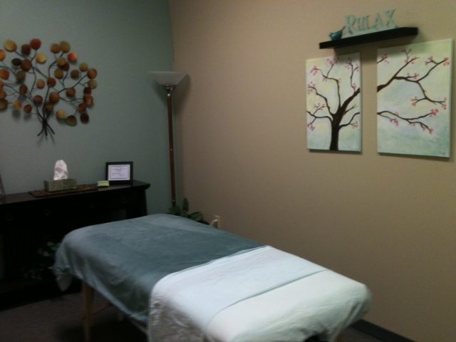 The massage room with a massage table, soft lighting and tree artwork on the wall